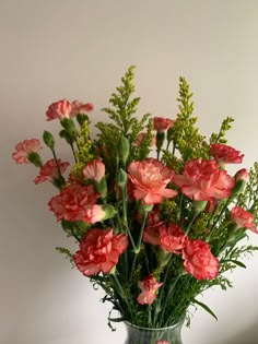 a vase filled with pink flowers on top of a wooden table next to a white wall