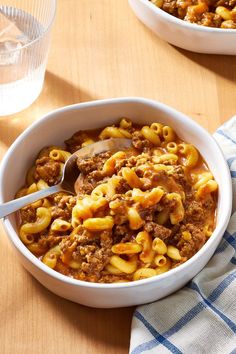 two bowls of chili macaroni and cheese with a spoon in them on a wooden table