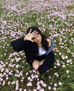 a woman sitting in the middle of a field of flowers with her hands on her head