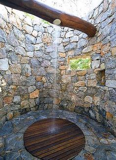 an outdoor shower with stone walls and wood flooring is seen in this image from the inside