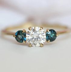 three stone engagement ring with blue and white topazs on the side, set in yellow gold