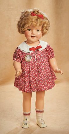 an old doll with blonde hair wearing a red dress and white collared shirt is standing in front of a beige background