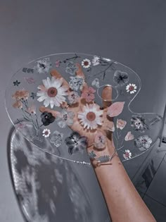 a person holding flowers on top of a glass table with silver legs and arms, in front of a gray background