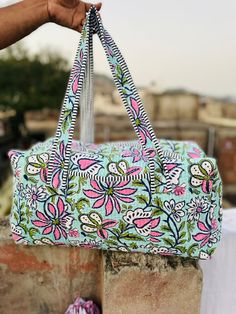 a hand holding a blue and pink floral print purse on top of a brick wall