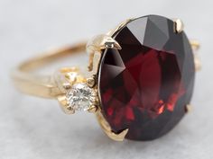 "This ring features a simple and classically designed mounting, the structural openwork shoulders lend a sense of light and grace to the mounting. Cut into a classic oval cut, the deep red cherry garnet in the center adds a lovely pop of color and also an interesting shape to a simple ring! Twinkling diamonds on either side of the stone add an extra bit of sparkle. Metal: 14K Yellow Gold Gem: Garnet 10.14 Carats Gem Measurements: 12.5 x 13.7 mm, Oval Accents: 2 Diamonds totaling .20 Carats, G in Color, VVS in Clarity  Ring Size: 4.25 Marks: \"14K\" Stamped on the inside band To view a video of this piece check out the link below: https://vimeo.com/839860918 SKU #: A26040 Each piece has been identified and graded by a Graduate Gemologist who has been certified by the Gemological Institute o Luxury Garnet Rings With Accent Stones, Elegant Multi-stone Garnet Rings, Gold Garnet Multi-stone Ring, Yellow Gold Garnet Multi-stone Ring, Diamond Ring Yellow Gold, Gold Garnet Ring, Pyrope Garnet, Garnet Rings With Polished Finish - Fine Jewelry, Garnet And Diamond Ring