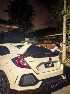 the rear end of a white car parked in front of a house at night time