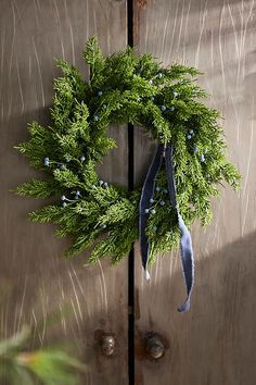 a green wreath hanging on the side of a wooden door with a blue ribbon around it