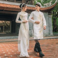 two people dressed in traditional chinese clothing standing next to each other on a brick walkway