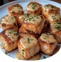 a white plate topped with sea scallops covered in gravy and garnished with parsley