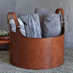 a brown leather basket filled with folded towels and other items sitting on top of a rug