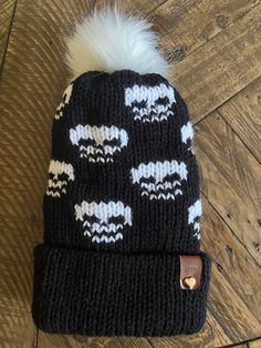 a black and white knitted beanie with sheeps on it sitting on a wooden floor