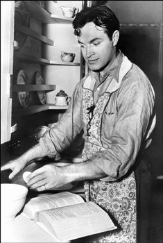 a black and white photo of a man in an apron working on a piece of paper