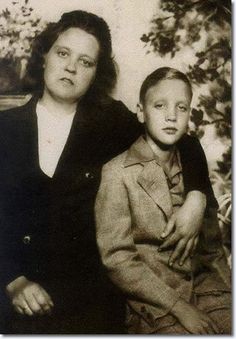 an old black and white photo of a woman sitting next to a young boy in a suit