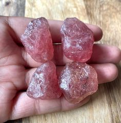 three pieces of pink colored rock sitting in the palm of someone's hand on a wooden table