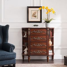 a blue chair sitting in front of a wooden cabinet with drawers and flowers on top