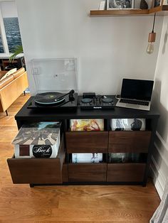 a record player sitting on top of a wooden shelf next to a laptop computer and records