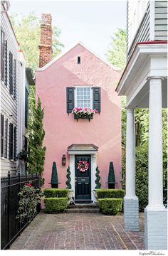 a pink house with black shutters and white trim on the front door is surrounded by greenery