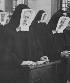 black and white photograph of women in nun robes with pictures on their heads sitting at desks