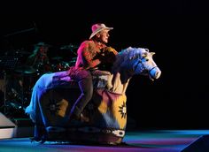 a man riding on the back of a white horse in front of a stage set