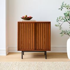 a wooden cabinet sitting on top of a hard wood floor next to a white vase