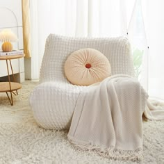 a white bed with a round pillow on top of it next to a table and lamp