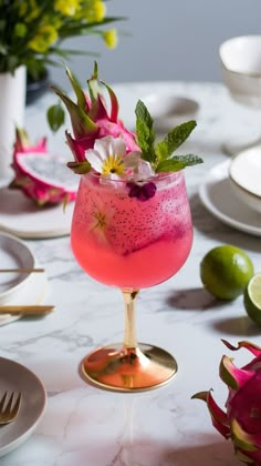 a pink drink with flowers in it sitting on a table next to plates and silverware