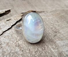 An elegant crystal white large oval Rainbow Moonstone has been set in sterling silver with a handmade ring band from sterling silver half dome wire. This moonstone is pearly white and shines on its own with hues of pink, blue, and even orange. The luminescent quality of the moonstone makes this ring beautifully unique and elegant. The stone is 13mm x 18mm in size with varying heights depending on the chosen stone. This is a closed setting-the back is not open. The stone sits in a solid sterling Oval Large Stone Moonstone Wedding Ring, Oval Moonstone Ring With Large Stone In Sterling Silver, Large Oval Moonstone Ring, Large Oval White Moonstone Ring, White Oval Moonstone Ring With Large Stone, Oval Moonstone Crystal Ring With Natural Stones, Adjustable White Oval Crystal Ring, White Moonstone Opal Ring In Oval Cabochon Shape, White Oval Crystal Gemstone Ring