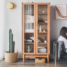 a woman sitting on a chair in front of a book shelf next to a cactus