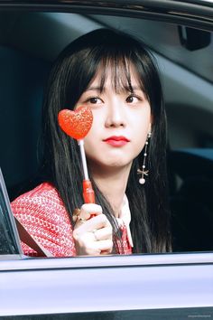 a woman holding a heart shaped lollipop in her hand and looking out the window