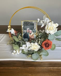 an arrangement of flowers and greenery on a table with a photo in the center