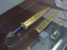 a gold and blue knife on display in a glass case with other items around it