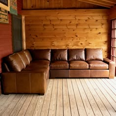 a brown leather couch sitting on top of a wooden floor in front of a window