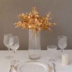 a white table topped with a vase filled with flowers and two glasses next to each other