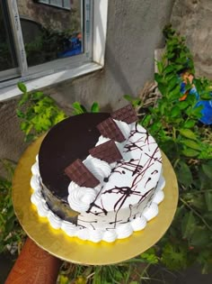 a cake sitting on top of a gold plate covered in white and chocolate frosting