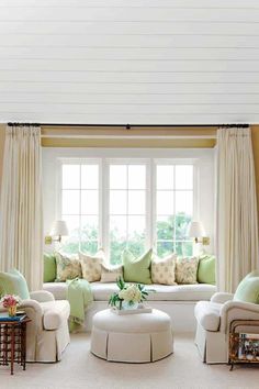 a living room filled with white furniture and lots of green pillows on the windowsill