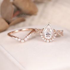 an engagement ring with a pear shaped diamond surrounded by small pearls on a white cloth