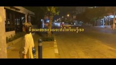 a young boy standing on the side of a road at night with words written in thai