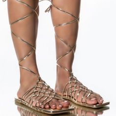 Flat Sandal In Gold Features A Vegan Leather Construction, A Flat Sole, A Strappy Lace Up Silhouette, An Open Square Toe, And A Wide Basket Woven Upper. Fit And Details Approx. Measured From A Women’s Size 8: - Open Toe - 35” Lace Length - Strappy Upper - Lace-Up Fit - Imported Gold Ankle Strap Lace-up Sandals For The Beach, Gold Strappy Sandals In Synthetic Material, Gold Strappy Synthetic Sandals, Gold Strappy Sandals For Vacation, Gold Strappy Lace-up Sandals For Vacation, Adjustable Gold Sandals For Beach Season, Gold Round Toe Lace-up Sandals For Vacation, Gold Ankle Strap Sandals For Beach Season, Gold Lace-up Sandals With Round Toe For Vacation