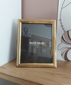 a gold framed photograph sitting on top of a wooden table next to a pink wall