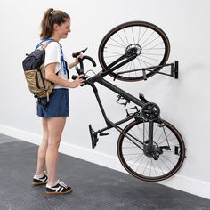 a woman standing in front of a bike mounted to the side of a white wall