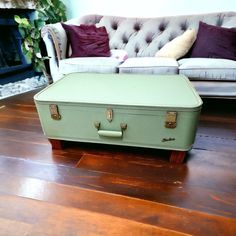 a green suitcase sitting on top of a wooden floor next to a couch and fire place