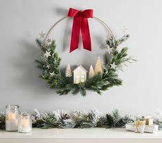 a christmas wreath hanging on the wall above a mantle with candles and other holiday decorations