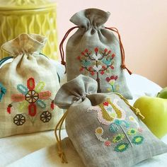 three bags with cross stitch designs on them sitting on a table next to an apple