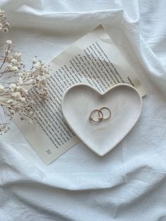 two wedding rings sitting on top of an open book next to some flowers and branches