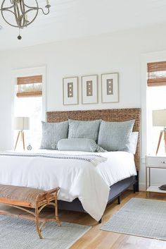 a bedroom with white walls and wood flooring has a large bed, wicker headboard, and two framed pictures on the wall