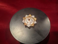 a black plate with a gold and white brooch on it's center, sitting on a red velvet surface