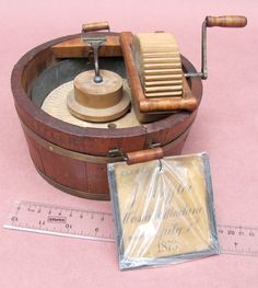 an old fashioned wooden spinning wheel with a ruler next to it on a pink surface