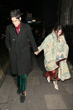 a man and woman holding hands walking down the street at night with one wearing a long coat