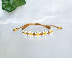 a white and yellow beaded bracelet on a white surface next to a green leaf