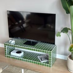 a flat screen tv sitting on top of a green tiled entertainment center next to a potted plant